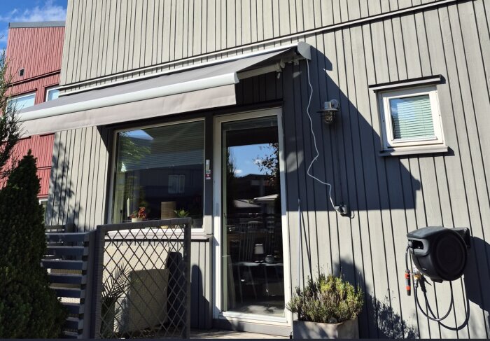 Terrassmarkis monterad över en altandörr, med elledning kopplad från fasadbelysning och en trädgårdsslangvinda monterad på väggen.