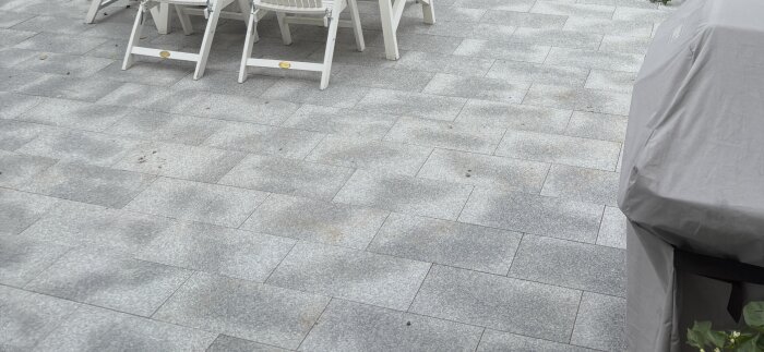 Fuktiga granithällar på en uteplats under en vit trädgårdsstol och täckt grill.