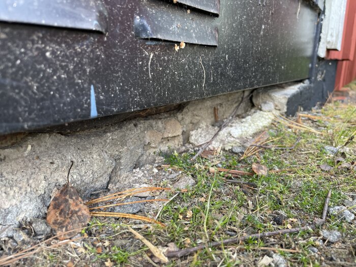 Spruckna skikt vid garagets fundament med lös isolering och synlig spricka mellan betongplattan och yttre delen av konstruktionen.