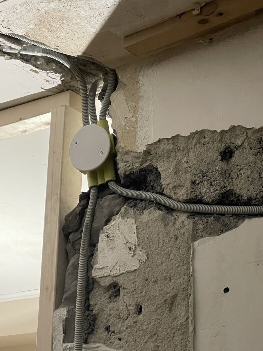 Gul kopplingsdosa som sticker ut från en bilad del av en vägg, med synliga elrör och ett vitt lock i nivå med väggen.