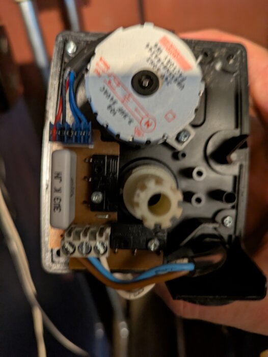 Närbild på en elektrisk motor med kablar och en kretskortskomponent, delvis synliga etiketter och anslutningar.