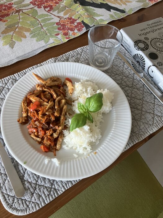 Tallrik med strimlat fläsk i bbq-sås, vitlök, ingefära, riven morot, lök, paprika, och ris, toppat med basilika, på en duk.