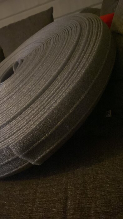 Rulle av grått, skummaterial liknande isolering eller tejp, placerad på en brun yta, oklart exakt användningsområde eller namn.