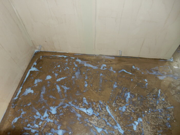 Bilden visar ett badrumsgolv med applicerat tätskikt vid hörnet av två väggar som en del av en pågående badrumsrenovering.