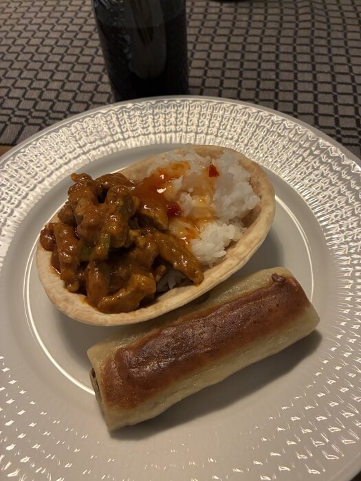 Tallrik med ris och pork-butter korma i brödkorg samt en vårrulle bredvid.