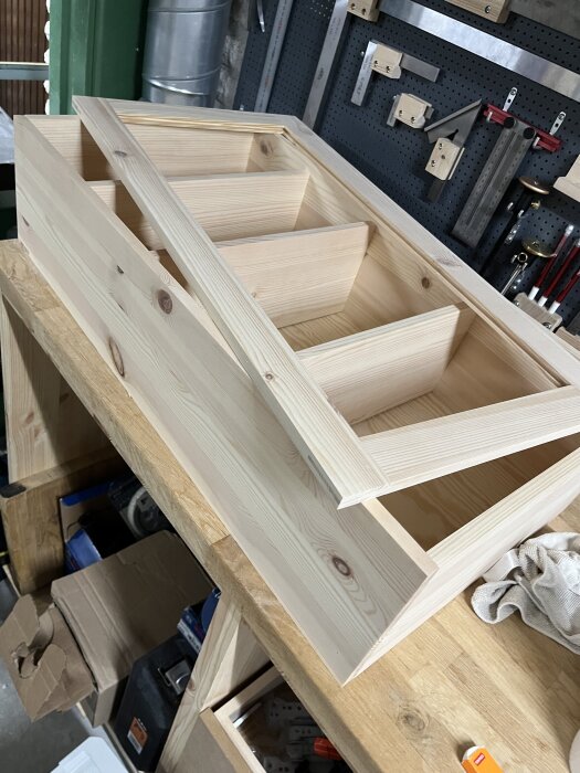 Furusnickeri i form av ett litet skåp med spegelram av plywood på en arbetsbänk, omgiven av verktyg i ett snickeri.