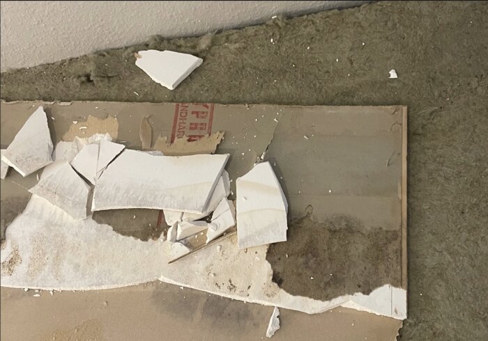 Brutna gipsskivor med fuktfläckar staplade ovanpå isoleringsmaterial.