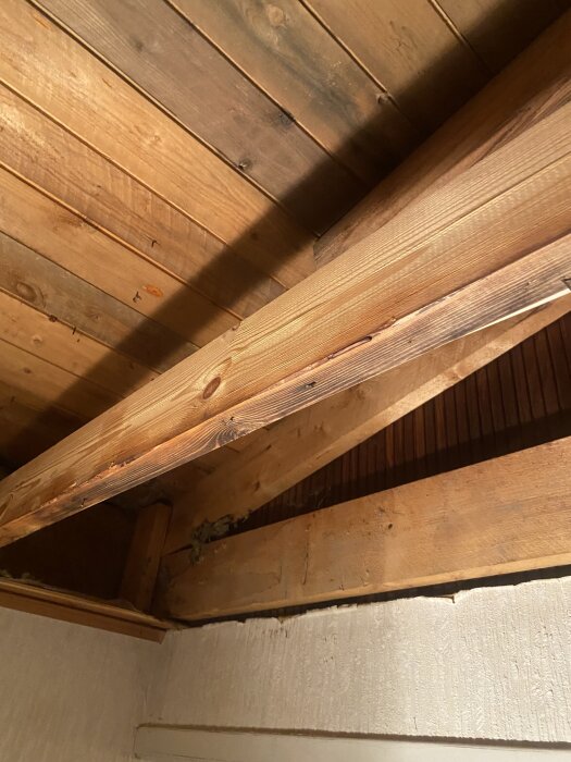 Fuktskadad träbalk och takpanel i interiör, visar effekter av fukt på byggmaterial.