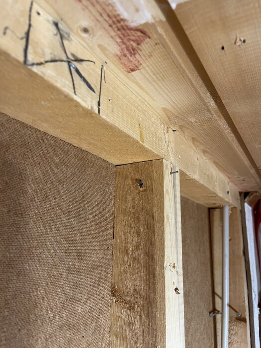 Träram med reglar och isolering i en vägg, med synliga markeringar och spikar, del av ett byggprojekt för att justera taköppningen.