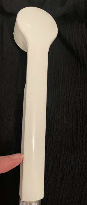 Vit munstycke med finger som pekar på platsen där en orange ring sitter, mot en mörk bakgrund.