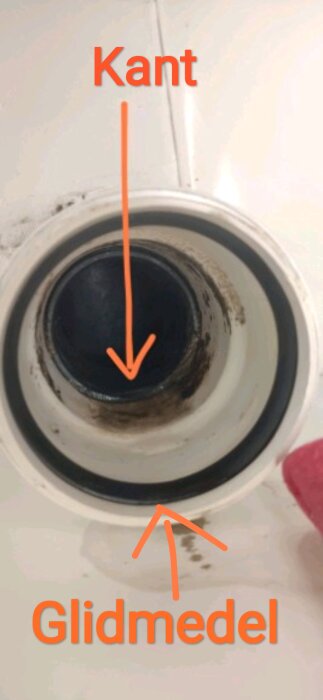 Avloppsrörsöppning med markeringar för kant och glidmedel, med delar av röret synliga inuti.