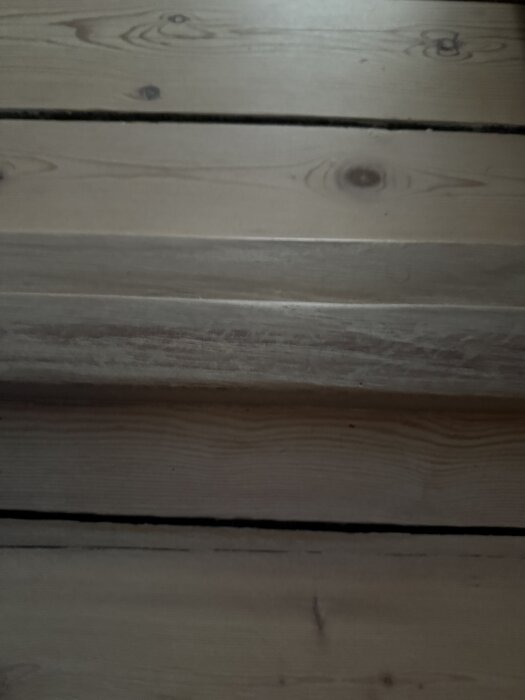 Närbild av ett slipat furugolv med synliga ådringar och några ojämnheter; hårdvaxoljan verkar flaga på vissa ställen.