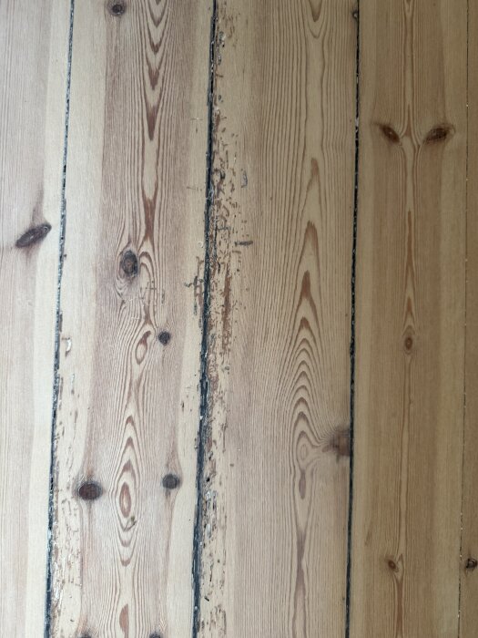 Gammalt furugolv med svarta springor, delvis slitet och med ojämn slipning samt hårdvaxoljan som flagnar på vissa ställen.