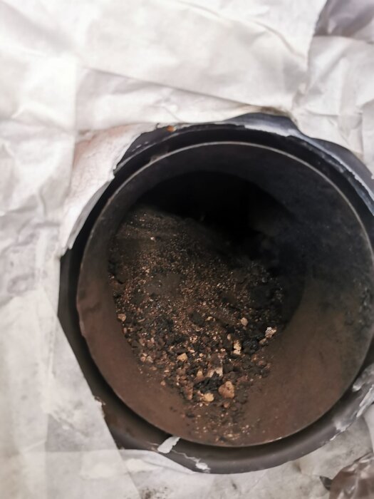 Sot och gammalt murbruk inuti en skorsten, sedd genom ett rör omgivet av trasig tejp eller papper.