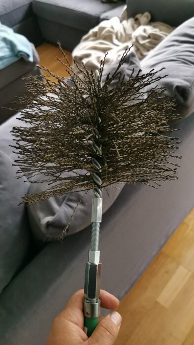 Cleaning brush for chimney duct held above wooden floor and grey couch.