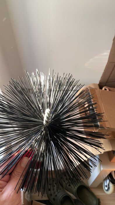 Hand holding a chimney brush with stiff bristles, used for cleaning soot and lime mortar buildup inside a chimney or duct.