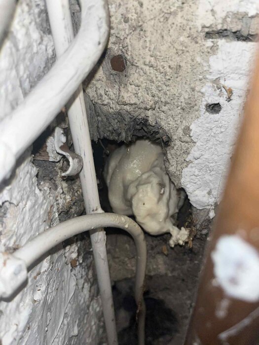 Hål i innertak med blågråa fibrer från innertakets skiva synliga, omgivna av kablar och rör.