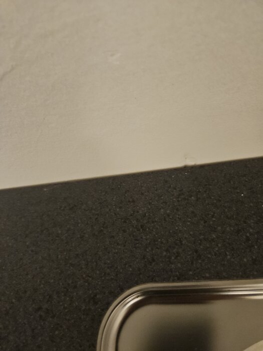 Svart bänkskiva monterad mot vit vägg i kök med liten spricka synlig mellan skiva och vägg.