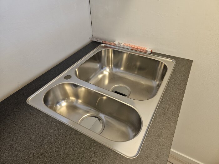Köksbänk med mörk bänkskiva där en dubbel diskho i rostfritt stål är installerad, med glipa mot väggen bakom.