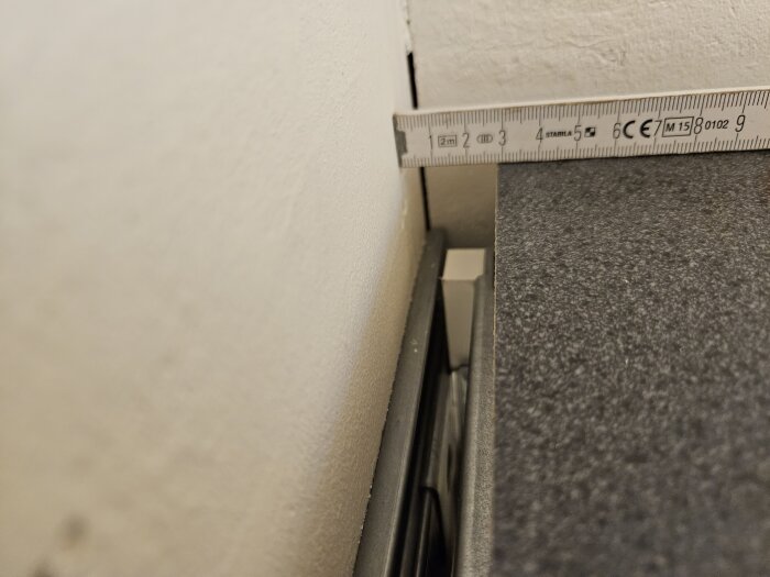 Måttband mäter avståndet mellan en köksbänkskiva och väggen. Glipan är cirka 20 mm, vilket skapar ett visuellt problem vid montering.