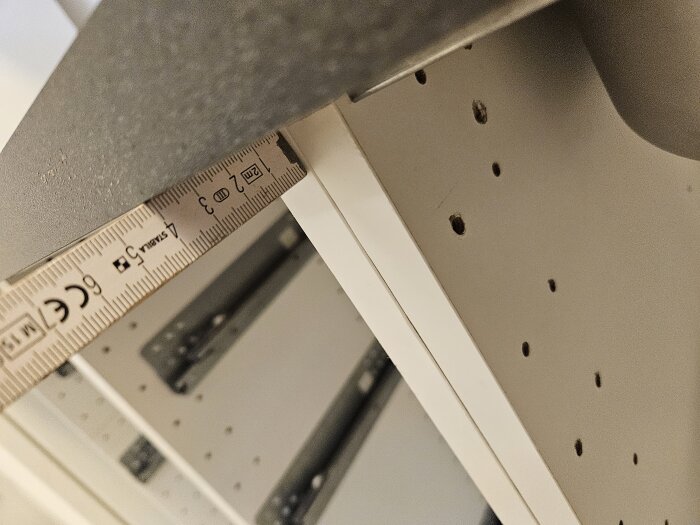 Närbild av en grå bänkskiva där avståndet till kanten mäts med linjal mot ett skåp med förborrade hål.