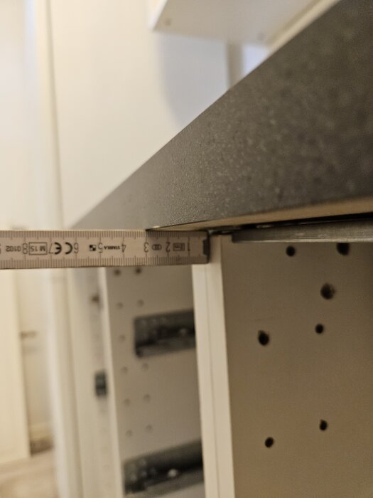 Mäta avstånd mellan bänkskiva och vägg i kök, med linjal som visar glipan.