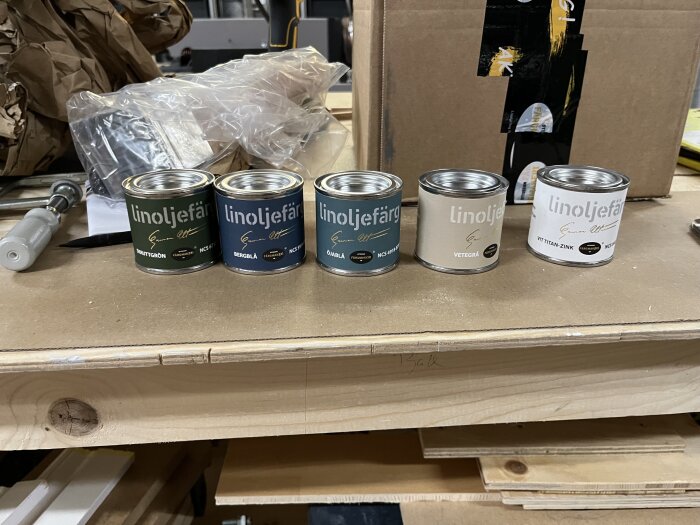 Flera burkar linoljefärg i olika nyanser står uppradade på en arbetsbänk, redo för färgval till ett köksprojekt.