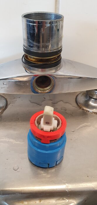 Blå och röd insats med vit komponent, nära en blandare. Insatsens form och dess montering verkar påverka funktionaliteten.