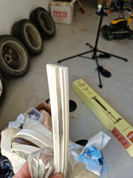 Dörrlist i närbild, hålls i handen, med bakgrund av föremål som däck och stativ i garage eller förråd.