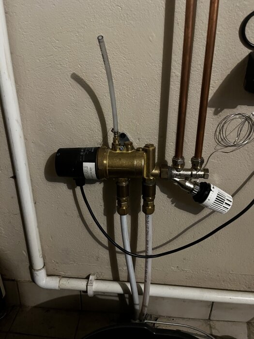 Rörsystem med tre kopparrör och en shuntventil monterad på en vägg, med diverse anslutningar och rördetaljer.