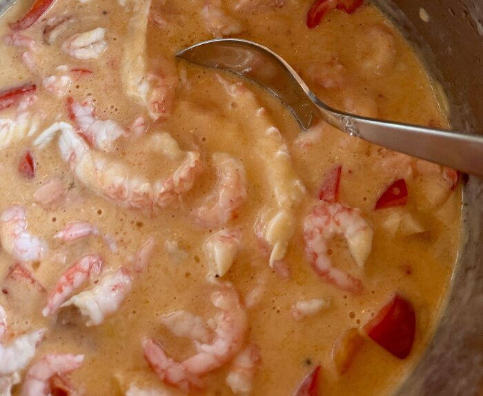 Fisk- och skaldjursgryta med räkor och kräftor i en krämig sås, serverad med en sked.