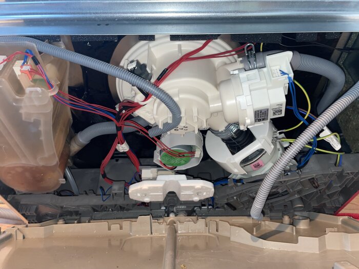 Öppen undersida av en Electrolux-diskmaskin med exponerade rör och kablar, inklusive en lös grå kabel till höger i bild.