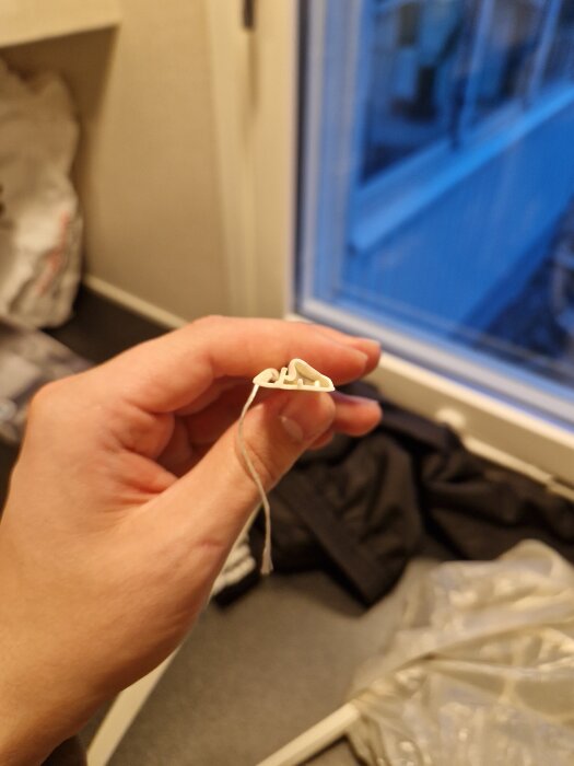 Hand håller en vit listprofil mot en bakgrund av ett fönster.