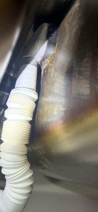 Närbild av läckage vid fästet av ett bräddavlopp på en diskho, visar rostbildning och anslutande avloppsrör.