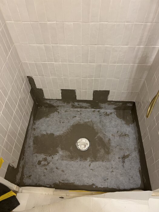 Golvbrunn omgiven av ny tätskiktsduk och limrester på golvet i en dusch, med synliga tätningsmaterial runt brunnens kanter.