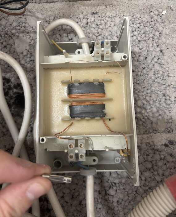 Bränd säkring i en 24-voltstransformator inuti en apparatlåda, med exponerade ledningar och komponenter, mot grå bakgrund.