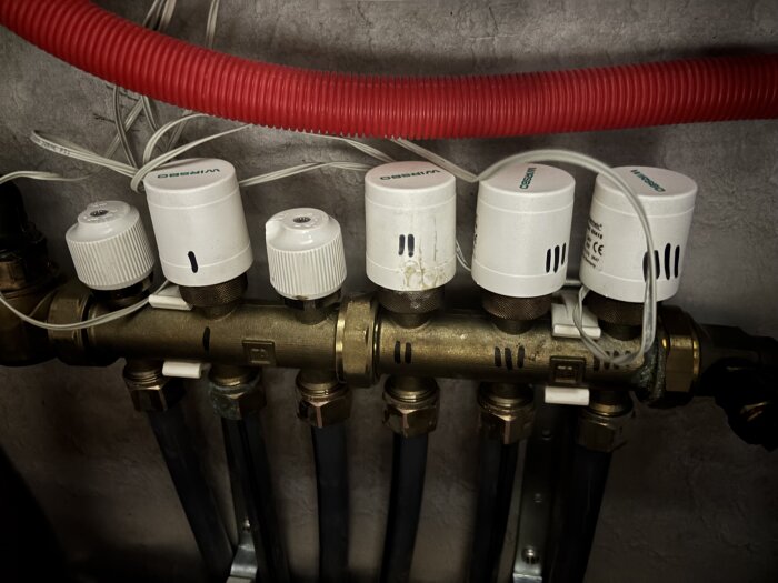 Elektriskt styrda Wirsbo thermatic ställdon monterade på ett rörsystem, med synliga ledningar och rör i en fastighet.