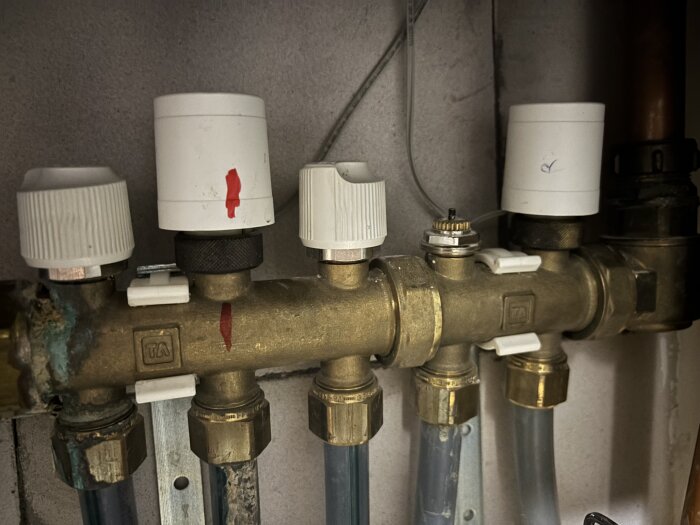 Bild av flera golvvärmeventiler installerade på kopparrör. Vissa ventiler har vita ställdon installerade ovanpå, inklusive tecken på slitage och korrosion.