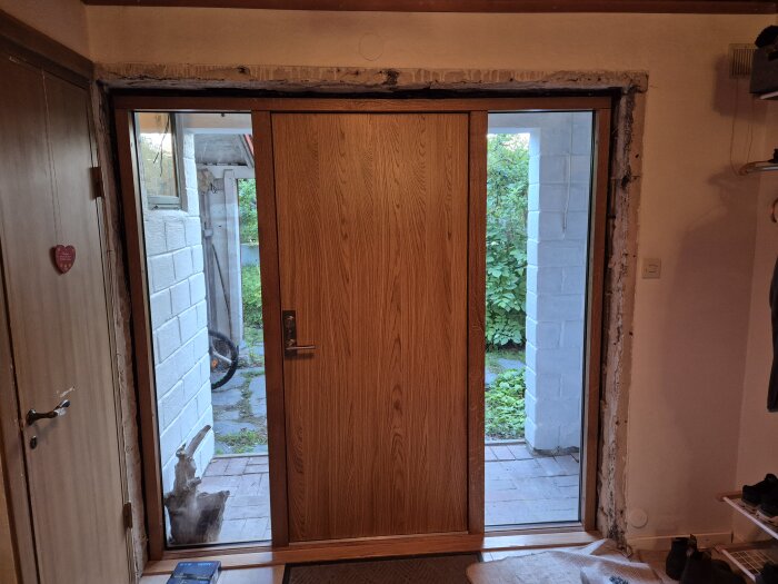 Nyinstallerad ytterdörr i trä med puts som behöver åtgärdas runt dörrkarmen på insidan av ett hus från 1940-talet.