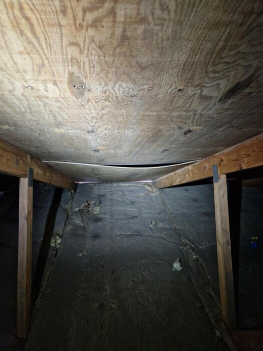 Plywoodskiva i taket synlig ovanifrån vinden, något hängande mellan reglar, vilket påverkar ventilationen i takkonstruktionen.