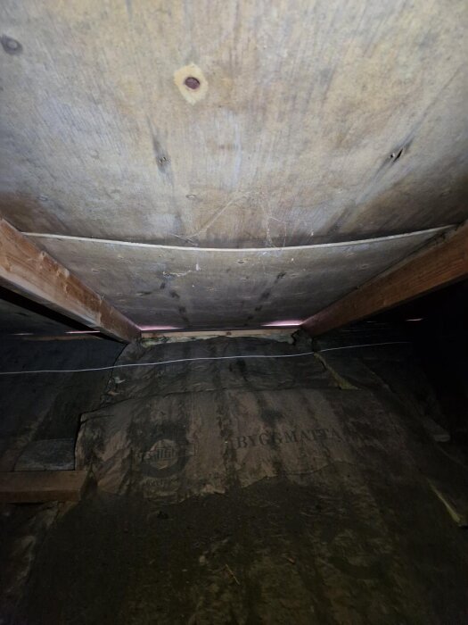 Plywoodtak på vinden som hänger ner, med träbalkar och isolering under taket.