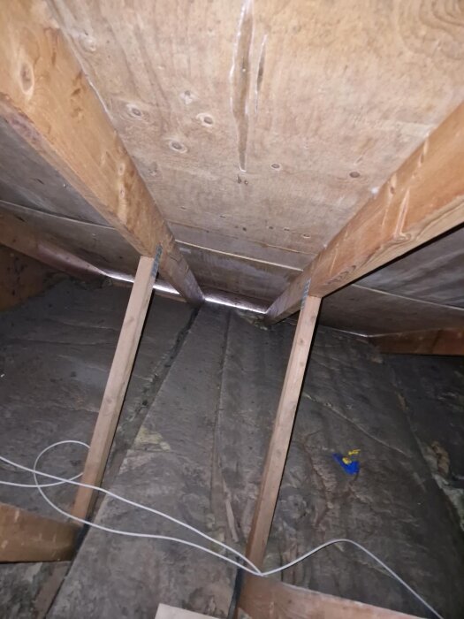 Plywoodtak i en vind med synliga reglar och hängande isolering.