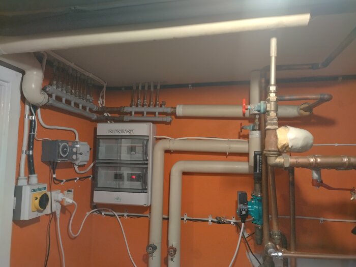 Rörsystem i hus från 1973 med värmepump Octopus Ispinne, visar ledningar och ventiler mot orange vägg.