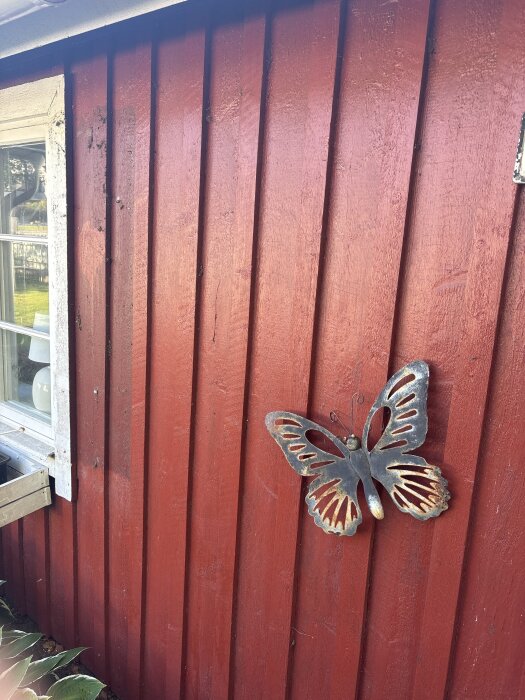 Röd träfasad med en metallfjäril och ett fönster på sidan.