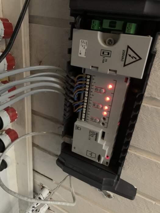 Smatrixenhet med blinkande lampor och flera anslutna kablar, monterad på en vägg intill andra elektriska komponenter.