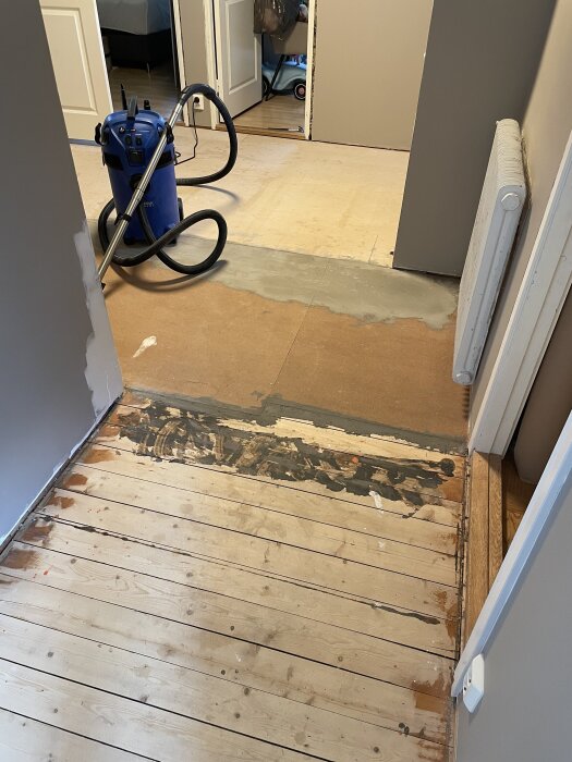 Bilden visar en hall med borttaget laminatgolv, en 22mm golvspånplatta och en blå grovdammsugare. Skillnad i golvhöjd syns tydligt.