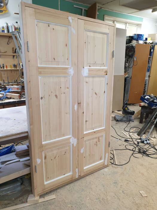 Pardörrar med karm och ektröskel i verkstad före vit lackering, omgivna av verktyg och byggmaterial.