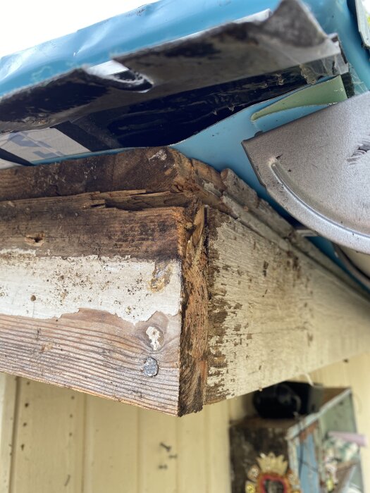 Närbild av en träbjälke med avskavd färg efter att vindskivorna tagits bort för målning, synlig takkant och del av vägg i bakgrunden.