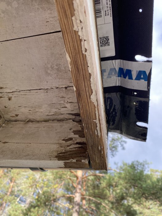 Slitna vindskivor som ska målas om, med skog i bakgrunden.