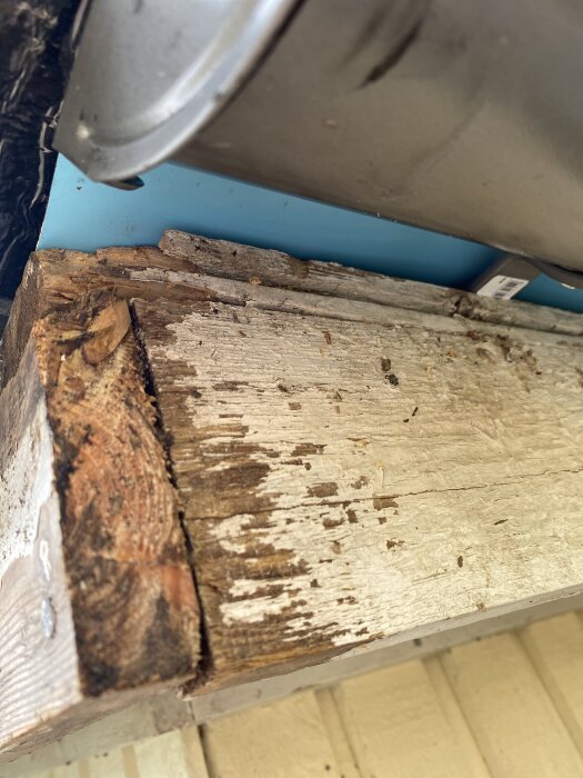 Gammalt trä och plåtkanter efter borttagna vindskivor inför målning, visar slitage och justering av skorstenens glipa.